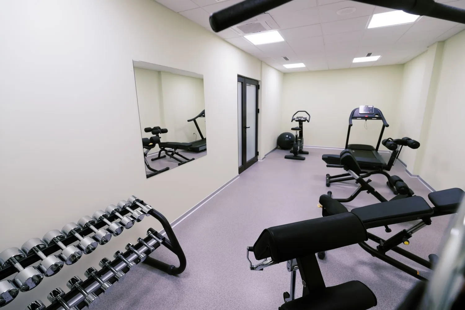 Gym mirrors Chicago example: a frameless wall mirror in a small fitness room with a dumbbell rack, benches and a treadmill
