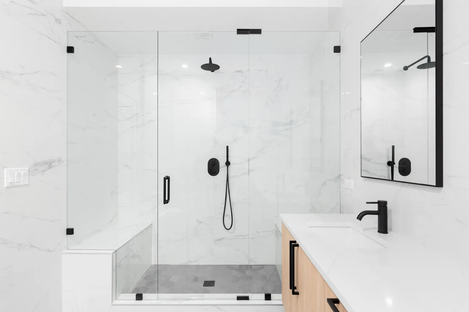 Frameless glass shower doors Chicago homeowners often choose: clear panels with matte black hinges and handle beside a marble bench
